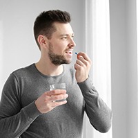 Young man taking a pill with a glass of water