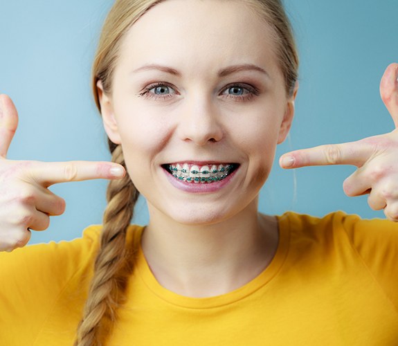 Woman with braces pointing to her smile